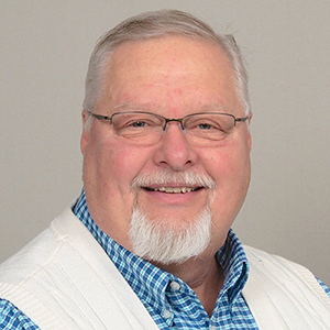 Smiling elderly man with glasses and white beard.