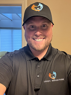 Smiling man wearing a black polo and cap indoors.